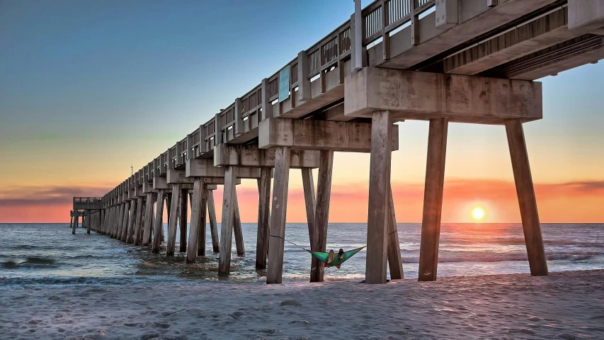 a man standing on top of a beach next to a pier, a digital rendering, by Brian Thomas, pexels contest winner, renaissance, the emerald coast, relaxing on the beach at sunset, hanging upside down, “the ultimate gigachad