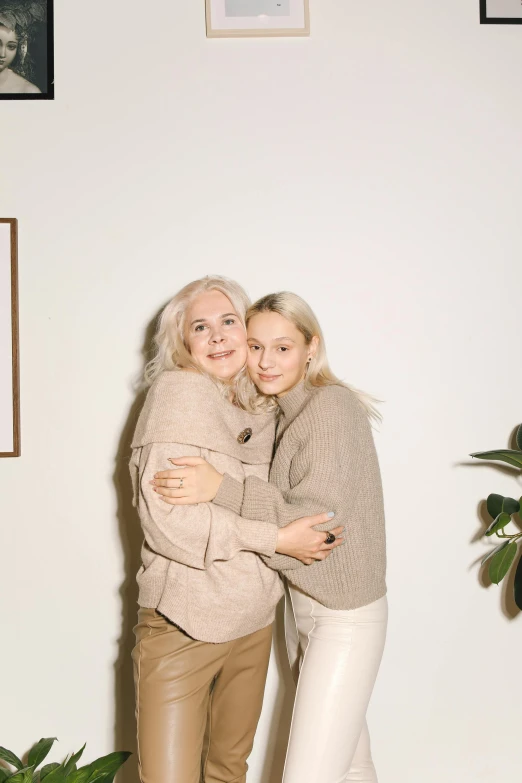 a couple of women standing next to each other, a picture, trending on pexels, white - blond hair, wearing a sweater, motherly, promotional image