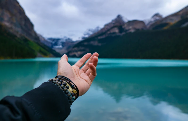 a person holding their hand out in front of a body of water, banff national park, onyx bracelets, healing, peace atmopshere