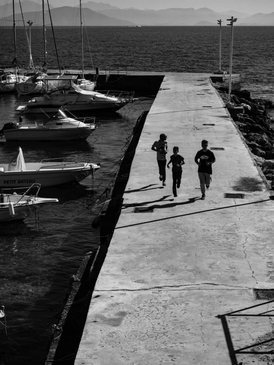 a group of people walking along a pier next to a body of water, by Alexis Grimou, three people running a marathon, high contrast light and shadows, christina kritkou, moored