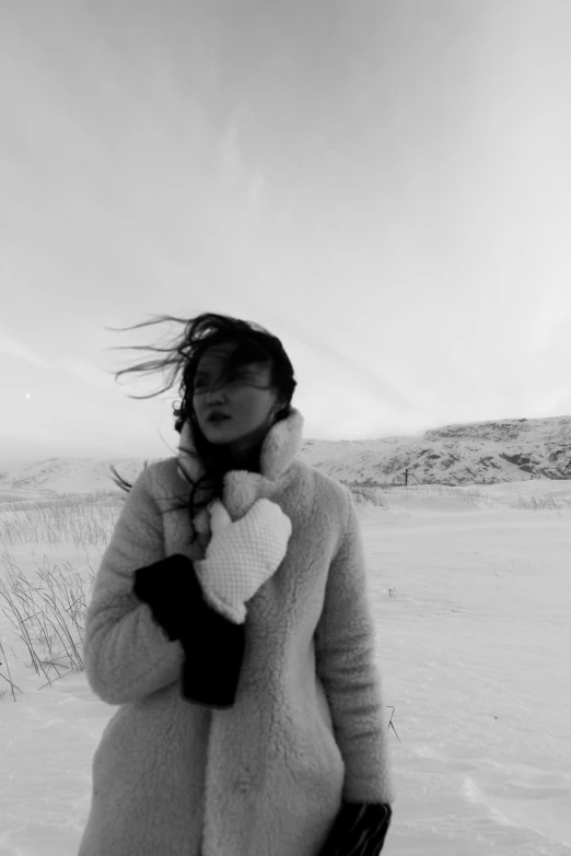 a black and white photo of a woman standing in the snow, inspired by Louisa Matthíasdóttir, charli xcx, windy beach, inuk, in a field