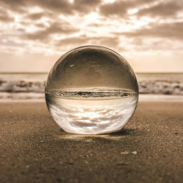 a glass ball sitting on top of a sandy beach, body of water