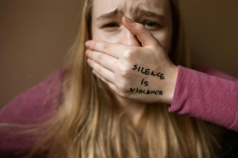a woman covering her face with the words silence is violence written on her hand, a picture, teenager girl, close up of a blonde woman, tape, grimacing