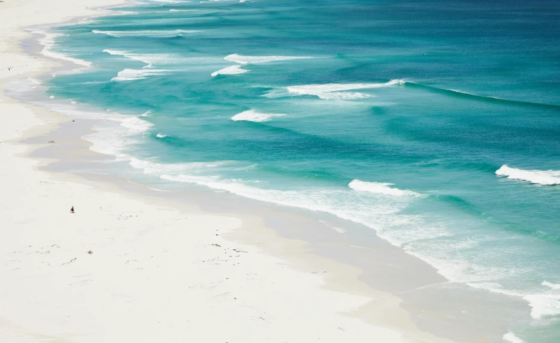 a large body of water next to a sandy beach, by Charlotte Harding, pexels contest winner, minimalism, white and teal metallic accents, south african coast, soaring waves, bleached colours