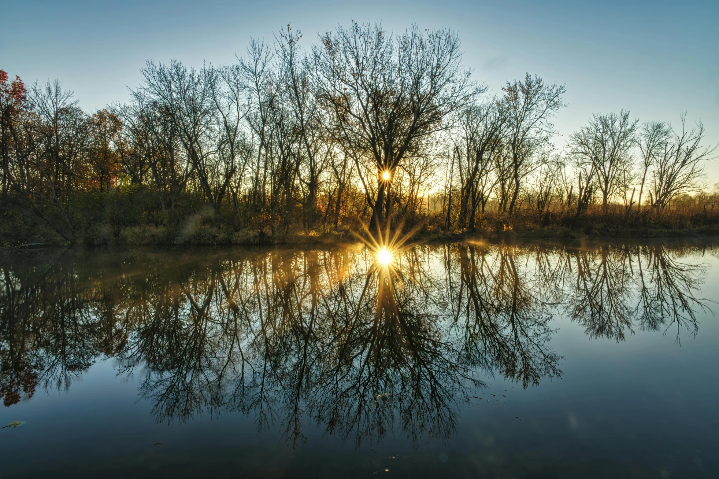 a large body of water surrounded by trees, by Brad Holland, pexels contest winner, land art, refracted sunset lighting, fan favorite, backlit, springtime morning