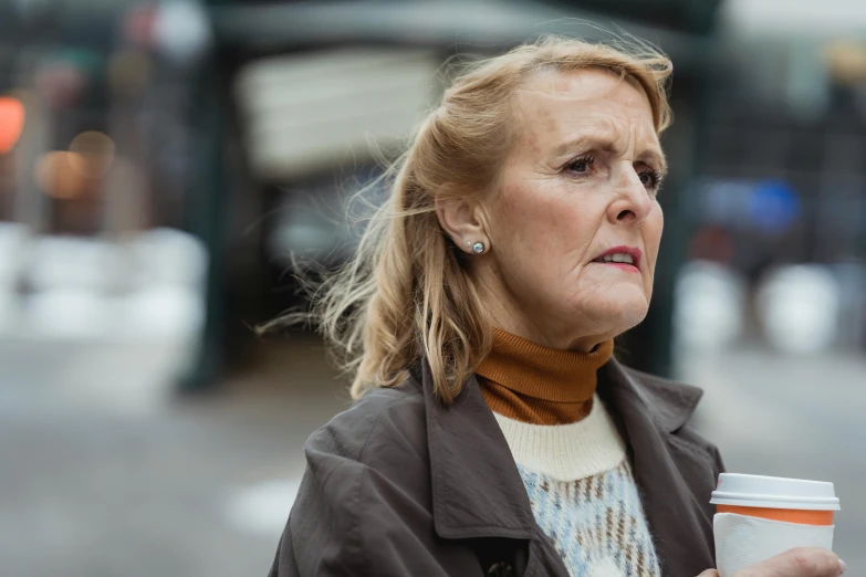 a woman holding a cup of coffee on a city street, a portrait, by David Begbie, trending on unsplash, photorealism, older woman, still image from tv series, minna sundberg, looking confused