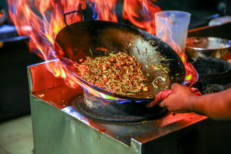 a person cooking food in a wok on a stove