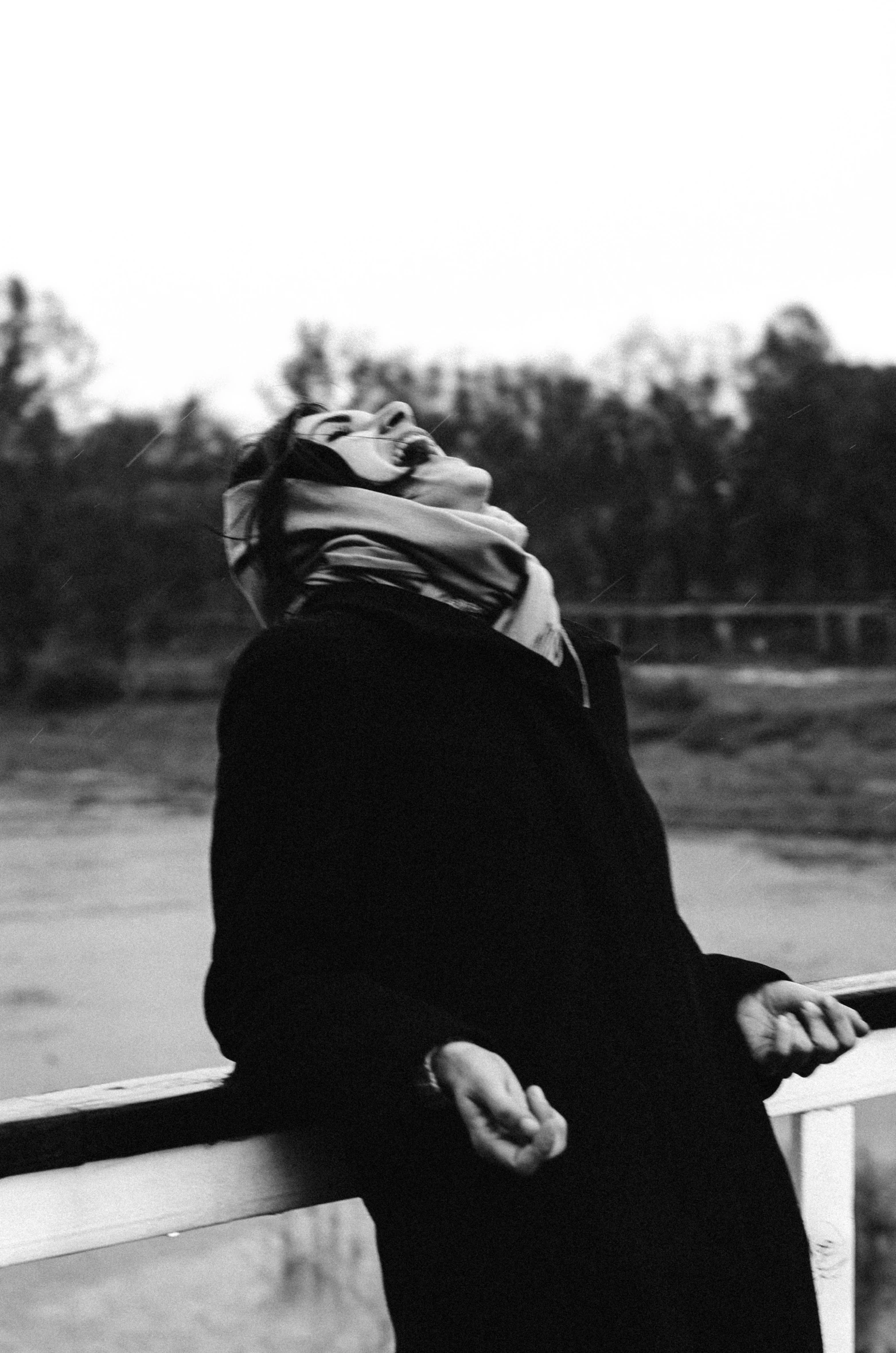 a black and white photo of a woman leaning against a railing, a black and white photo, unsplash, conceptual art, face is wrapped in a black scarf, yawning, river in front of him, androgyny