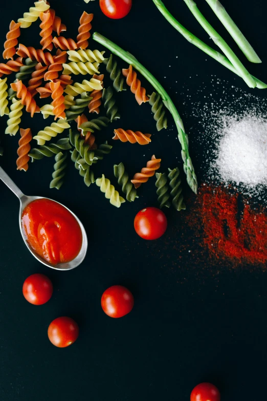 a table topped with pasta, asparagus and tomatoes, a still life, pexels contest winner, contrast colors, spatula, with a black background, ketchup