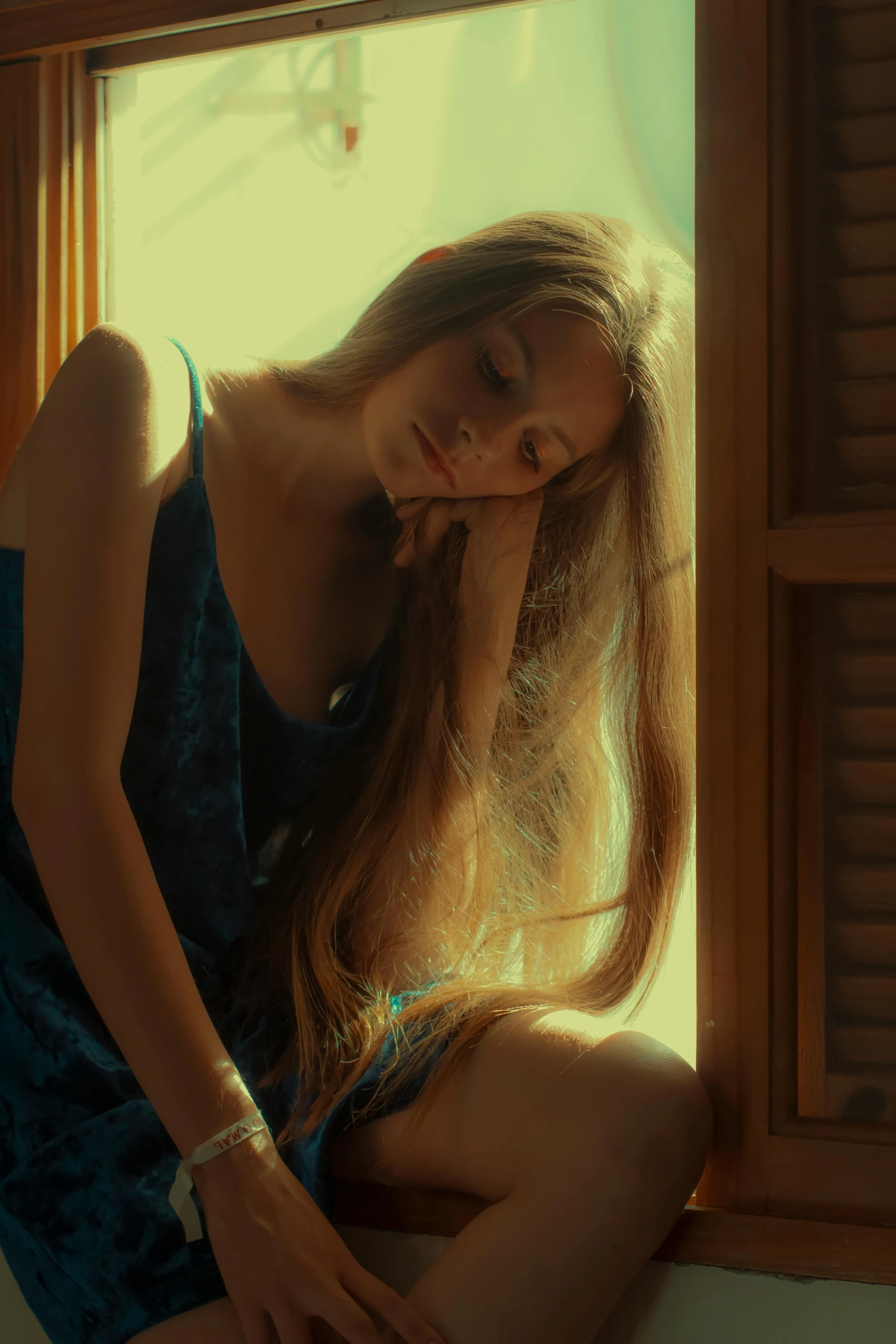 a woman in a blue dress sitting on a window sill, a picture, inspired by Elsa Bleda, pexels contest winner, renaissance, ilya kuvshinov with long hair, sleepy expression, blond brown long hair, standing in a dimly lit room