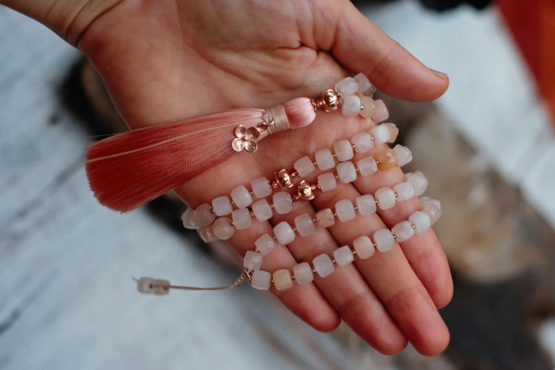 a person holding a bunch of beads in their hand, by Julia Pishtar, pexels, hurufiyya, pink zen style, dressing tassels gemstones, rectangle, moonstone