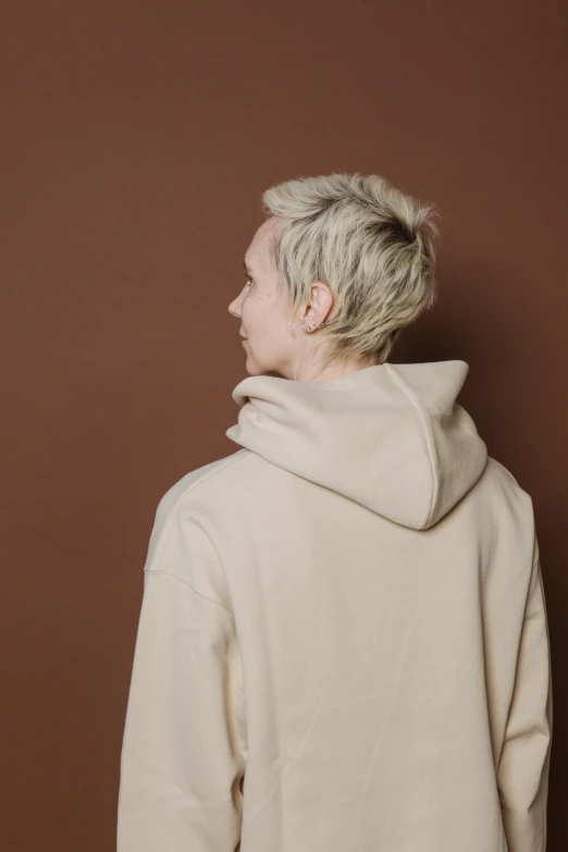 a man standing in front of a brown wall, an album cover, inspired by Josef Abel, trending on pexels, realism, beige hoodie, short platinum hair tomboy, facing away, kacper niepokolczycki