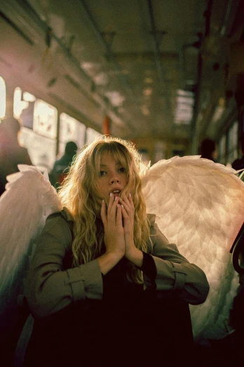 a woman with angel wings covering her face, an album cover, inspired by Nan Goldin, pexels contest winner, sydney sweeney, sat down in train aile, biblically accurate angels, cute girl