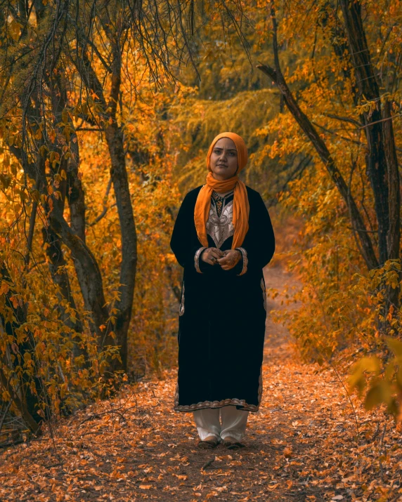 a woman standing in the middle of a forest, an album cover, inspired by Modest Urgell, pexels contest winner, hurufiyya, orange color, muslim, golden autumn, ((portrait))