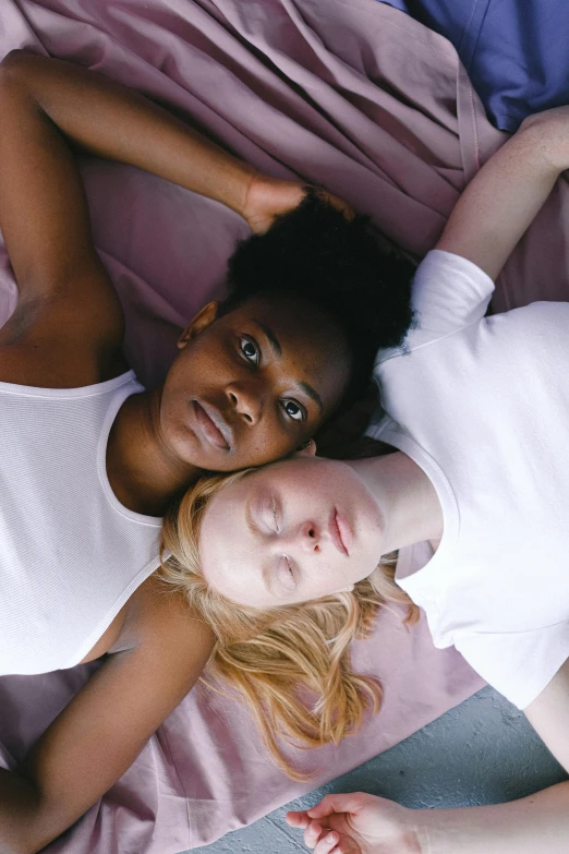 a couple of women laying on top of a bed, by Matija Jama, trending on pexels, renaissance, diverse faces, pale woman, beautiful highly symmetric faces, black teenage girl