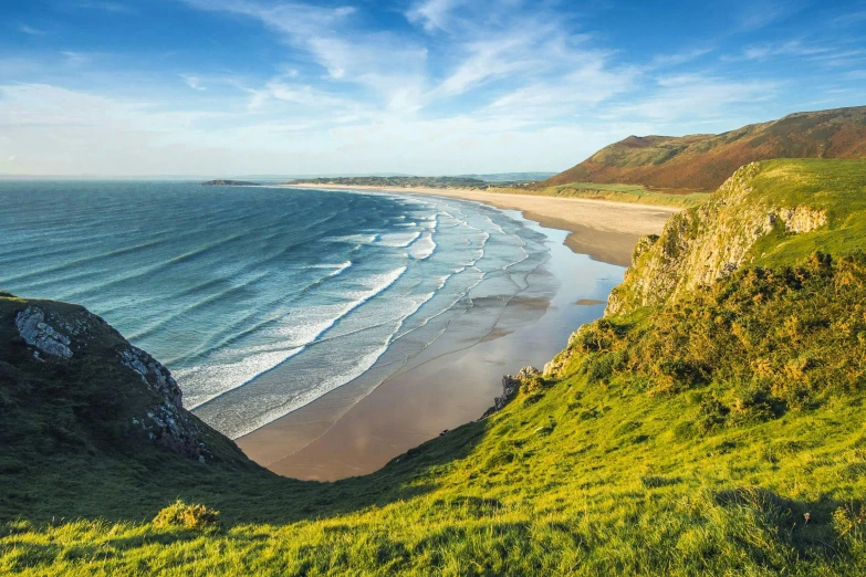 a view of a beach from the top of a hill, by Charlotte Harding, pexels contest winner, wales, sunny morning light, thumbnail, hills and ocean