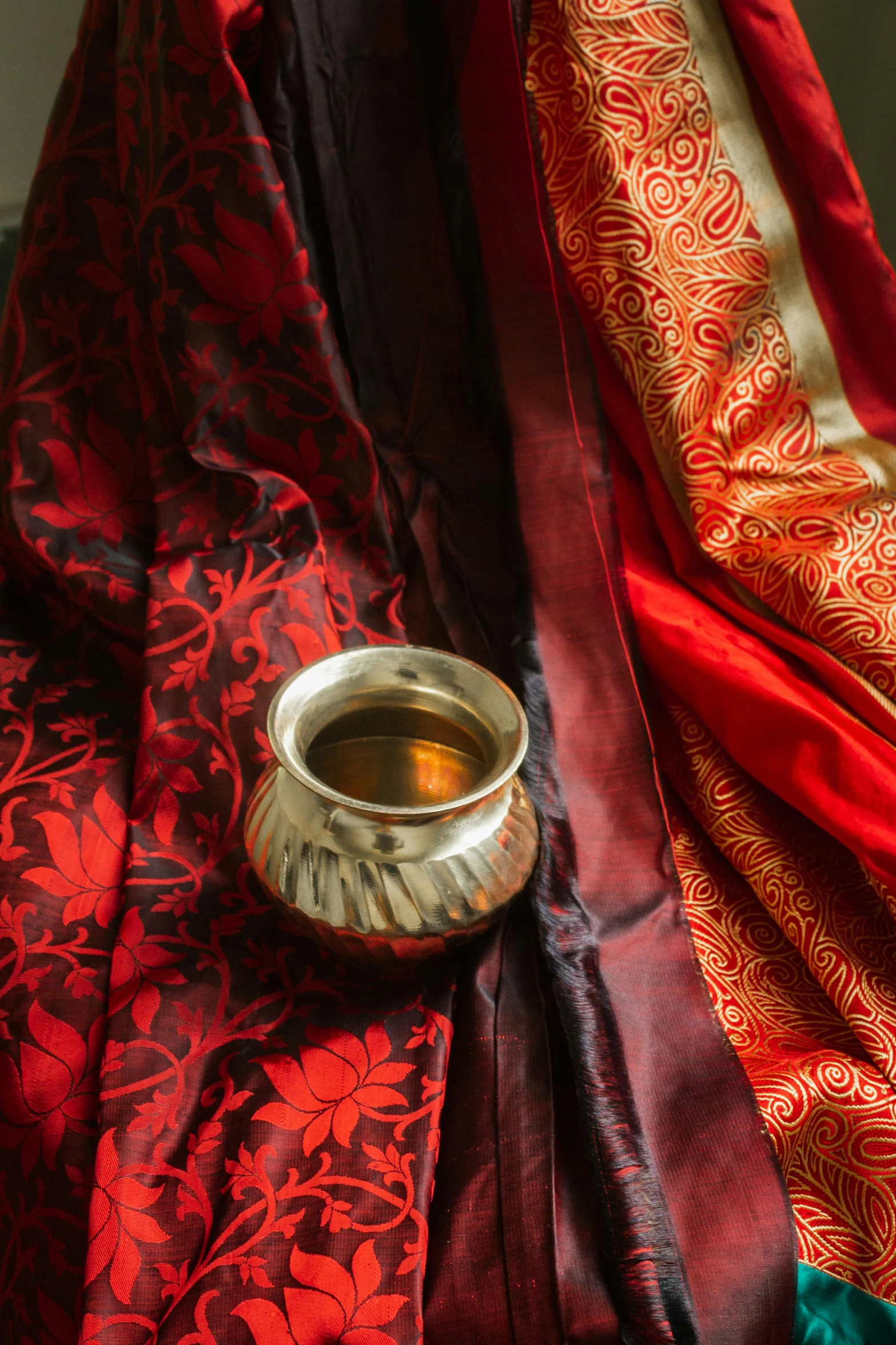 a cup of coffee sitting on top of a table, a still life, by Mardi Barrie, trending on unsplash, renaissance, dressed in a sari, red silk flowing fabric, cloth and metal, patterned clothing