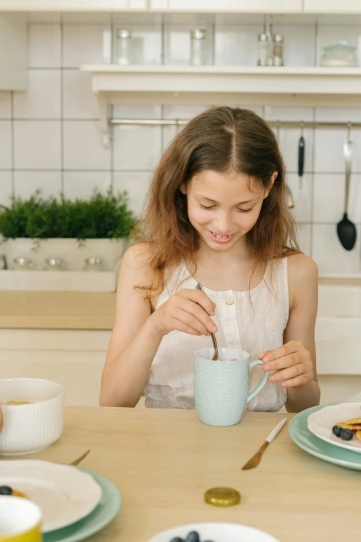 a woman sitting at a table eating breakfast, pexels contest winner, happy kid, with a white mug, teenager, cooking