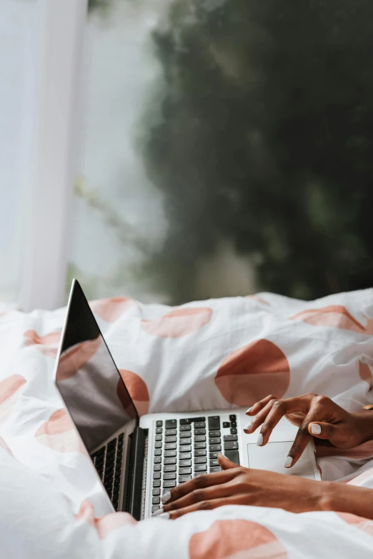 a woman laying in bed using a laptop computer, trending on pexels, happening, white and pink cloth, sleek hands, polka dot, professional image