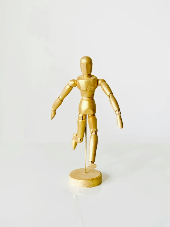 a wooden mannequin standing on a white surface, dancing a jig, accented in bright metallic gold, fully posable, 2019 trending photo