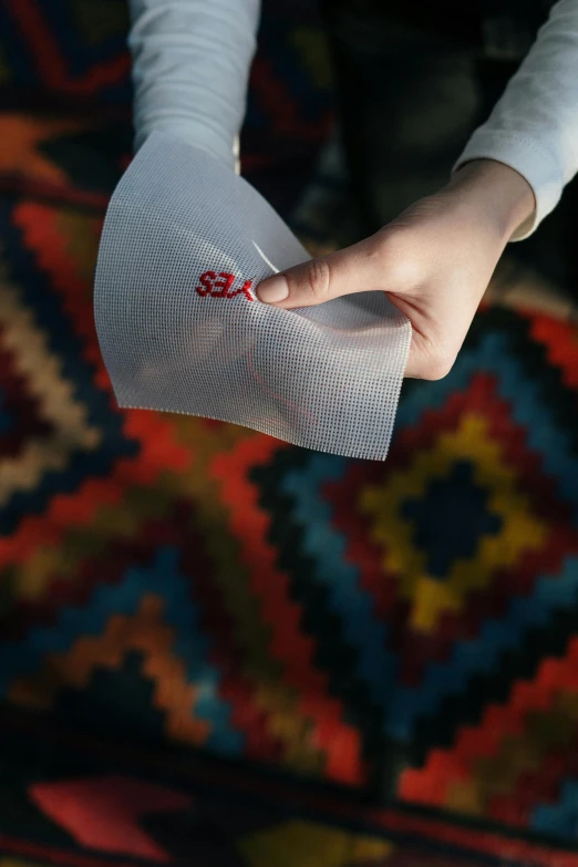 a close up of a person holding a piece of paper, a cross stitch, sket - one x iamretro, red fabric, rug, size