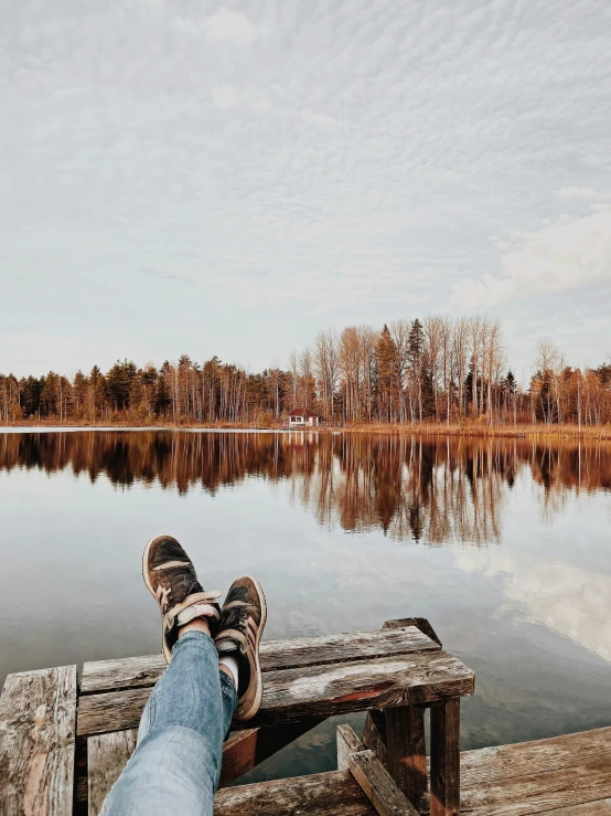 a person sitting on a bench next to a body of water, by Jaakko Mattila, pexels contest winner, duck shoes, panoramic shot, in fall, wideangle portrait