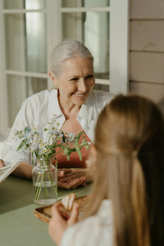 a group of people sitting around a table, flowers, older woman, family friendly, trending photo