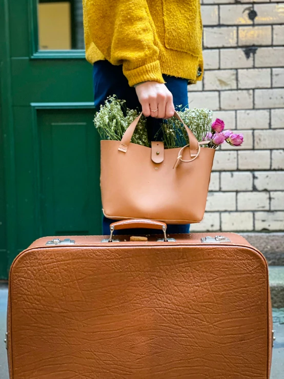 a woman standing next to a suitcase with flowers in it, by Julia Pishtar, pexels contest winner, leather pouch, light brown, thumbnail, multiple stories