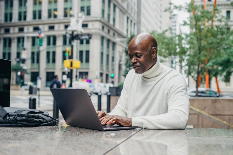 a man sitting at a table using a laptop computer, by Meredith Dillman, pexels contest winner, at a city street, african canadian, thumbnail, avatar image