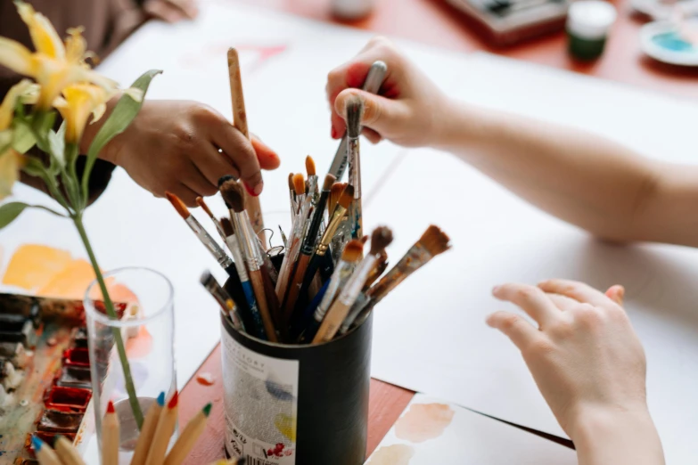 a group of people sitting at a table with paint brushes, pexels contest winner, holding pencil, trending art station, thumbnail, close-up photograph