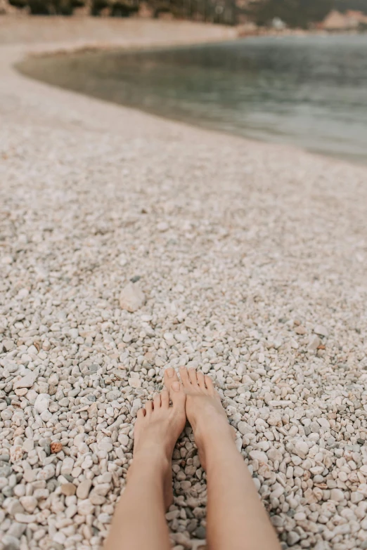 a person laying on a beach next to a body of water, trending on unsplash, renaissance, barefeet, pebbles, low quality photo, tan