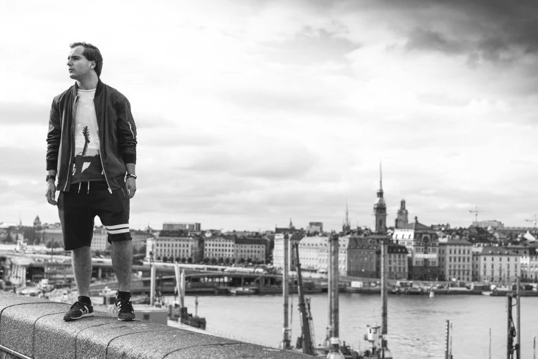 a man standing on top of a wall next to a river, a black and white photo, by Anato Finnstark, stockholm city, ed sheeran, jake gyllenhaal, nika maisuradze