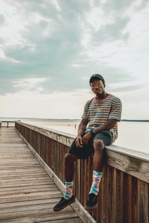 a man sitting on a dock next to a body of water, jaylen brown, multicolored, in savannah, full protrait