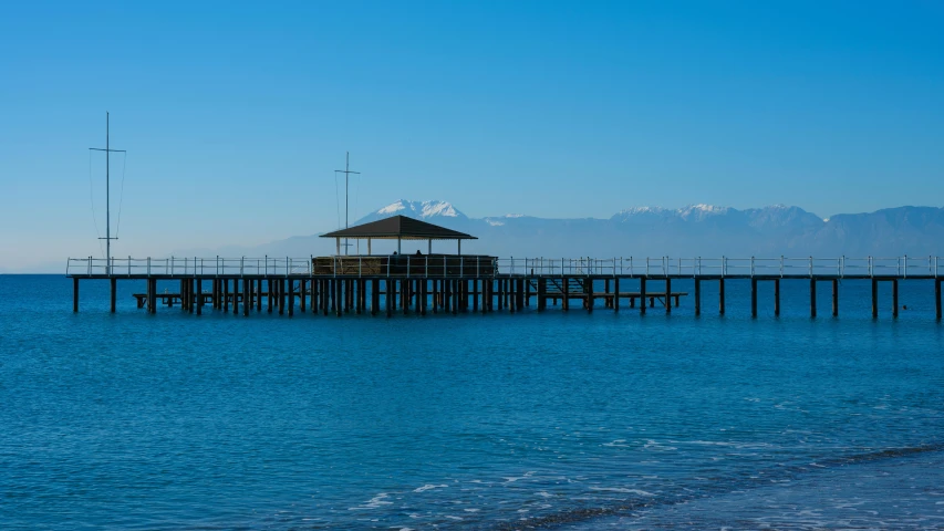 a pier in the middle of a body of water, hurufiyya, clear blue skies, mount olympus, high quality image”