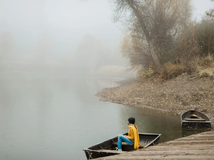 a woman sitting on a dock next to a body of water, by Béla Nagy Abodi, pexels contest winner, yellow volumetric fog, small boat, azamat khairov, fall season