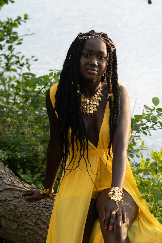 a woman in a yellow dress sitting on a log, inspired by Ras Akyem, pexels contest winner, afrofuturism, dreadlock black hair, pearls and gold chains, she is about 1 6 years old, dark black skin tone