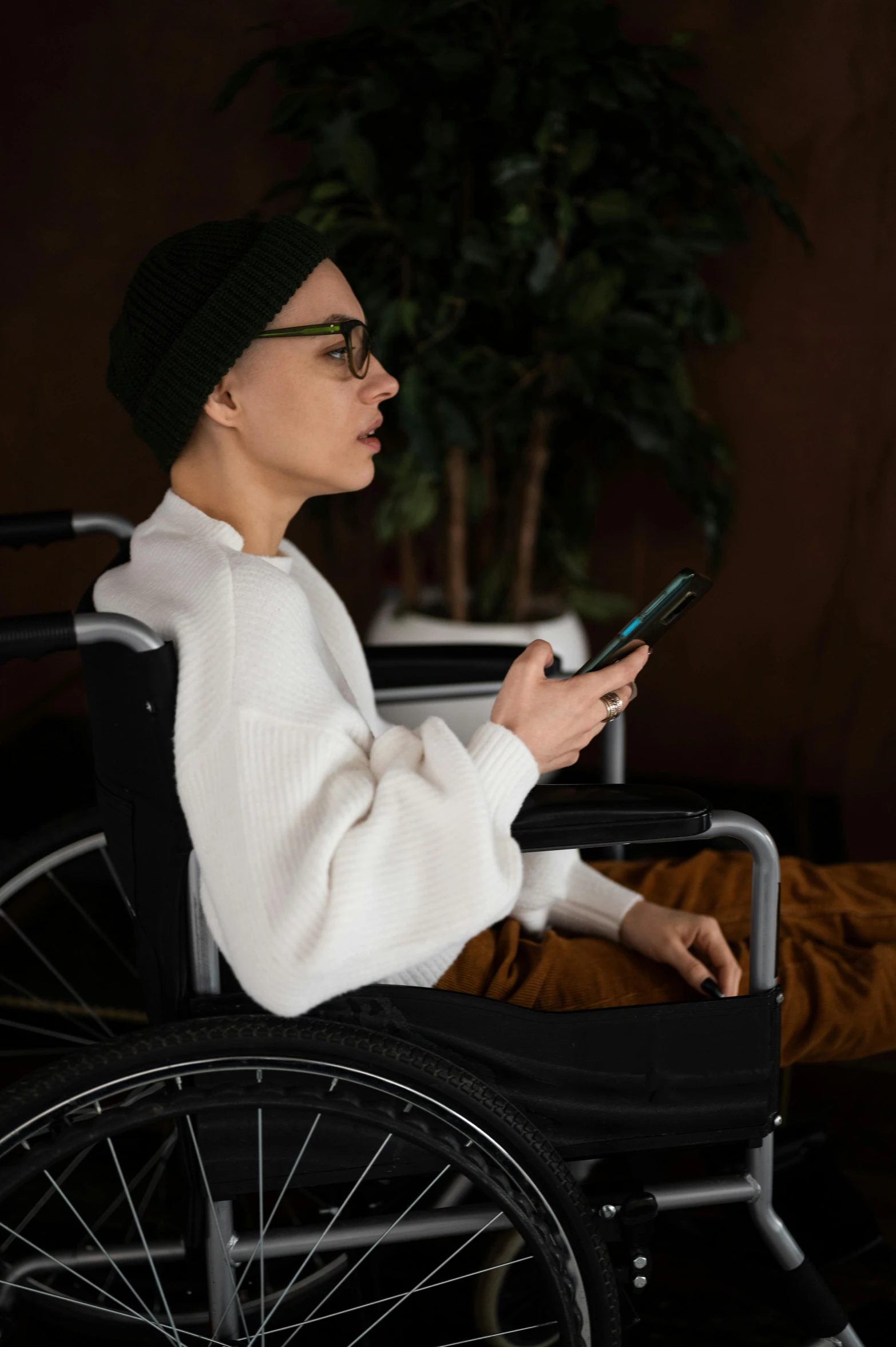 a woman in a wheelchair using a cell phone, by Adam Marczyński, trending on pexels, hurufiyya, square, androgynous person, hospital, with a long