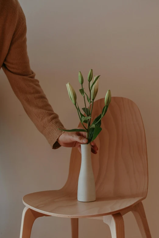 a person placing a flower in a vase on a chair, inspired by Sarah Lucas, trending on unsplash, minimalism, datura, low detail, made of wood, tall