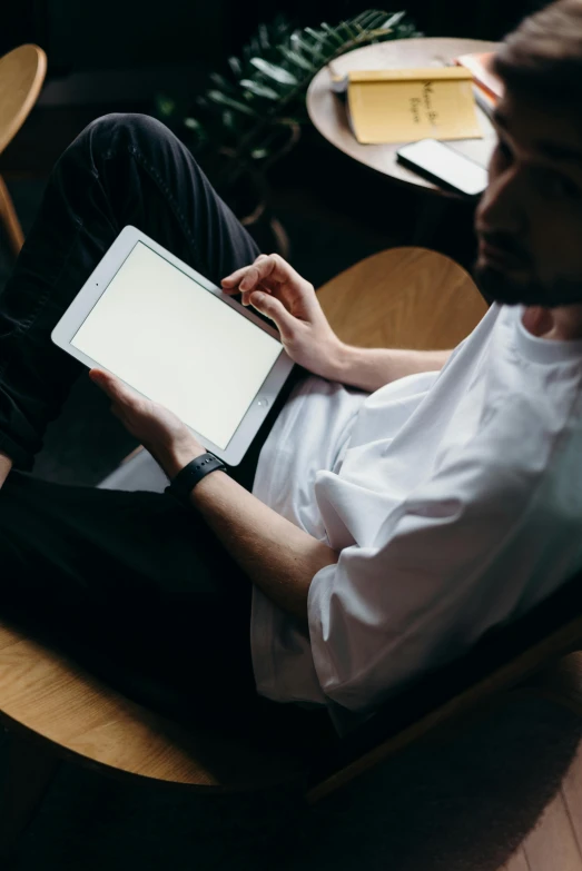 a man sitting in a chair using a tablet computer, trending on unsplash, wearing a white shirt, high angle shot, looking content, ilustration