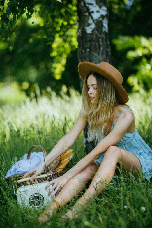 a woman sitting in the grass with a picnic basket, pexels contest winner, young southern woman, with hat, sydney park, blue