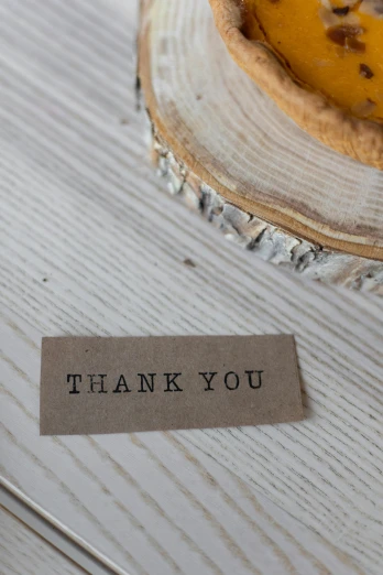 a piece of pie sitting on top of a wooden table, a picture, thank you, product label, detail shot, no text