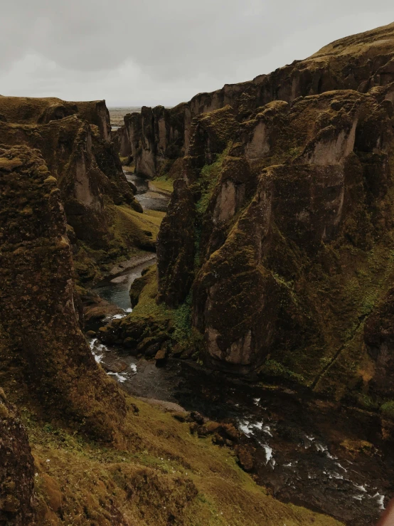 a man standing on top of a cliff next to a river, by Johannes Voss, pexels contest winner, renaissance, chiseled formations, in a valley, with lots of dark grey rocks, high view