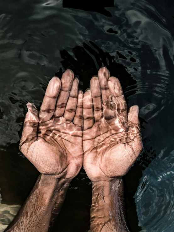 a person holding their hands in a body of water, brown skin like soil, his palms are sweaty, desaturated, shot with sony alpha