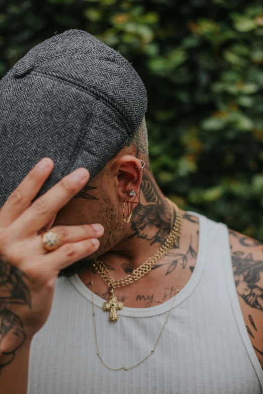 a close up of a person wearing a hat, a tattoo, inspired by L. A. Ring, trending on pexels, hear no evil, gold chains, holes in a religious man, praying with tobacco