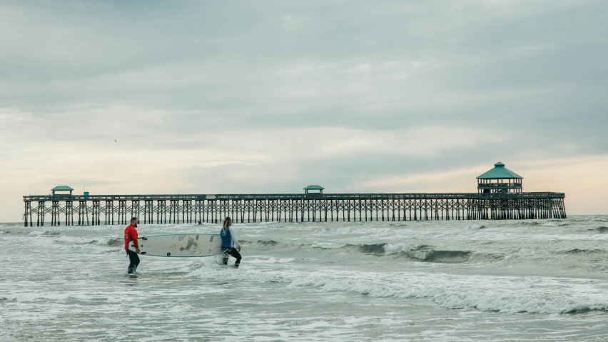 two surfers carrying their boards into the ocean, by Peter Churcher, unsplash contest winner, hurufiyya, walking on ice, near a jetty, families playing, playing soccer on the beach