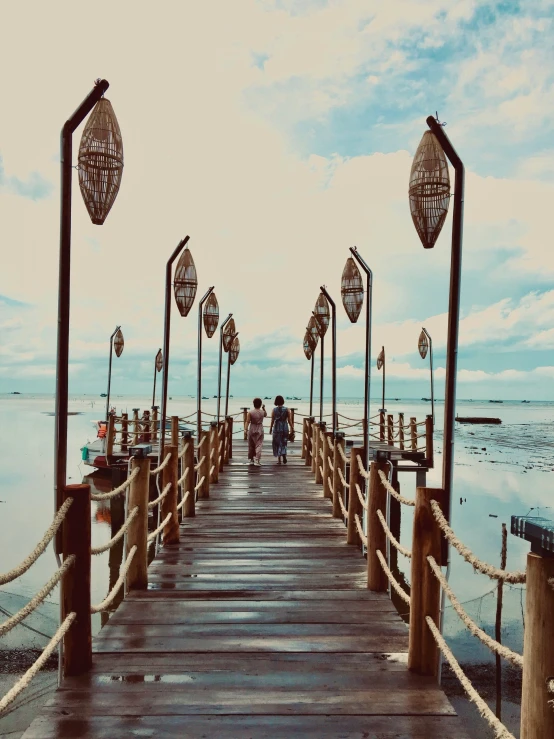 a wooden pier next to a body of water, a picture, by Robbie Trevino, sumatraism, hanging lanterns, walking towards camera, in a beachfront environment, vintage photo