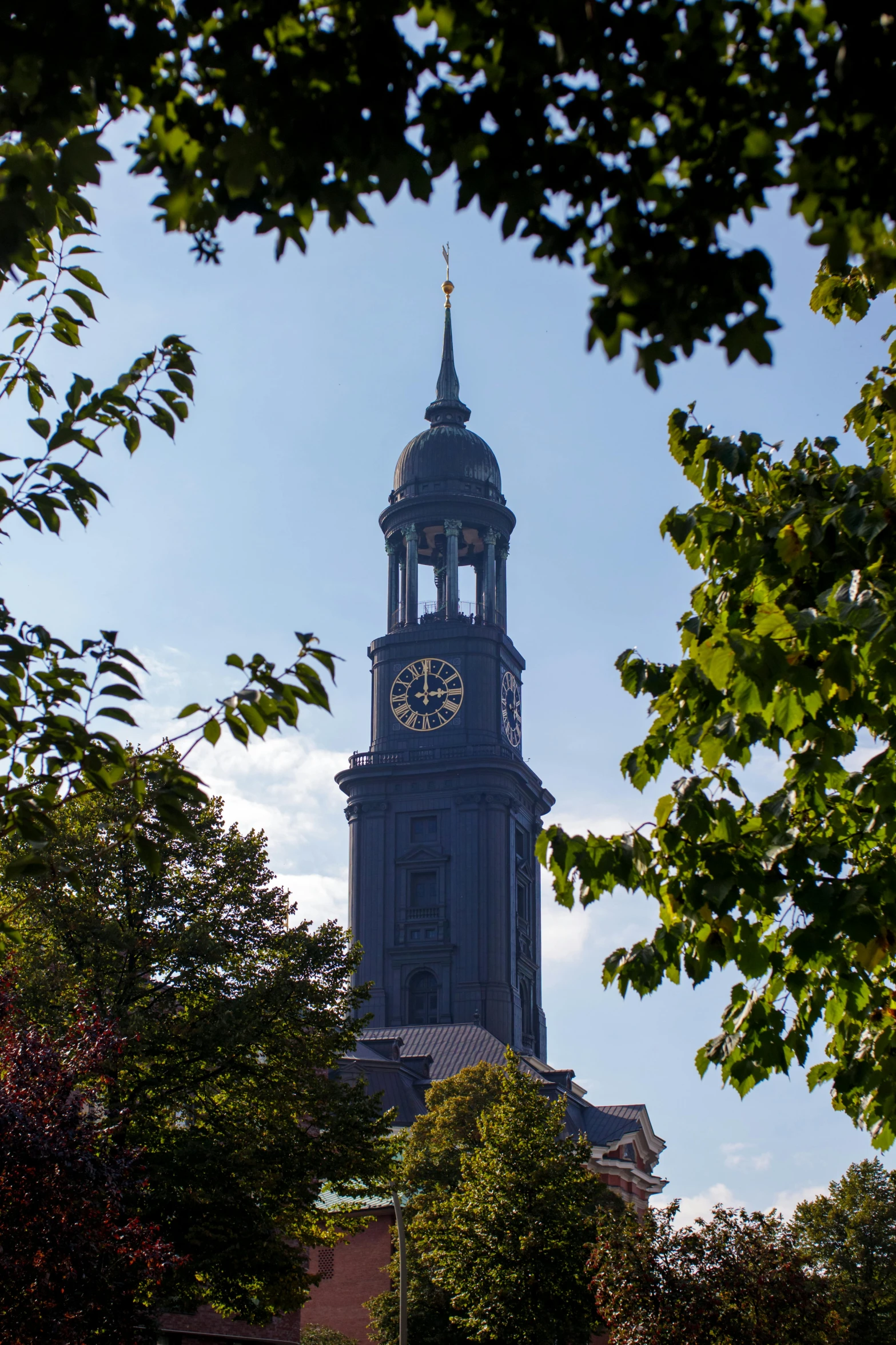 a clock that is on the side of a building, inspired by Abraham van den Tempel, heidelberg school, neoclassical tower with dome, with dark trees in foreground, lead - covered spire, taken in the early 2020s