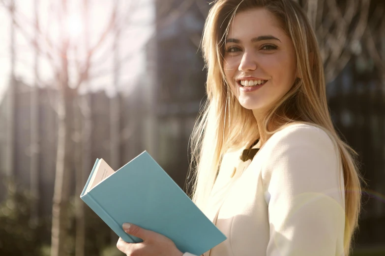 a close up of a person holding a book, beautiful and smiling, a girl with blonde hair, looking smart, in the sun