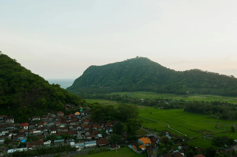 an aerial view of a village with a mountain in the background, pexels contest winner, sumatraism, ultrawide lens”, early evening, green, 8 k hi - res