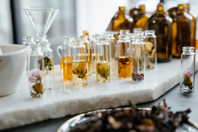 a table topped with bottles filled with different types of flowers, by Jessie Algie, trending on unsplash, process art, beakers full of liquid, miniature product photo, amber, close up half body shot